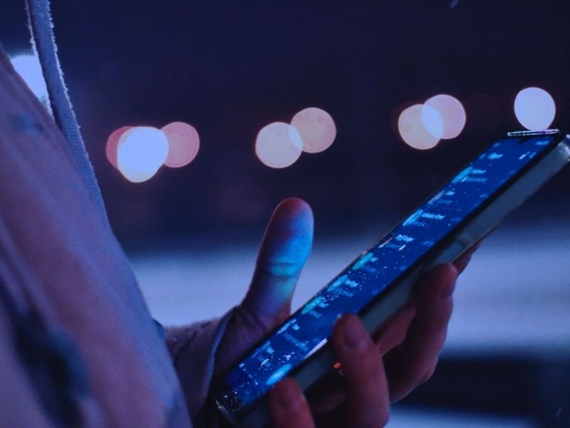 Close-up de mão segurando smartphone iluminado pelas luzes da cidade durante a noite